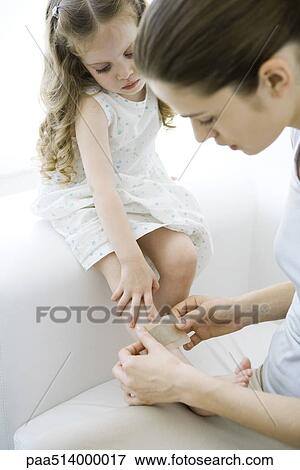 Mother putting adhesive bandage on young daughter's leg View Large Photo Image Stock Photo - Mother putting adhesive bandage on young daughter's leg. Fotosearch