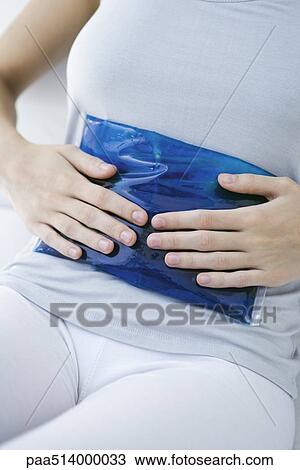 Stock Image - Woman holding ice pack against her stomach, cropped view. Fotosearch