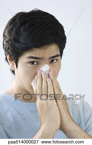 Stock Photo - Young man blowing his nose, looking at camera. Fotosearch