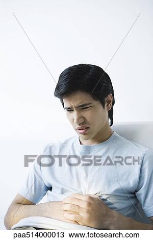 Young man holding his stomach and furrowing his brow View Large Photo Image Stock Image - Young man holding his stomach and furrowing his brow. Fotosearch