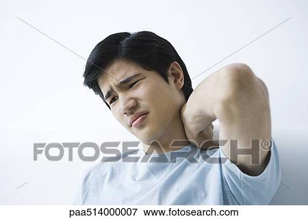 Young man holding neck, furrowing brow View Large Photo Image Stock Photo - Young man holding neck, furrowing brow. Fotosearch