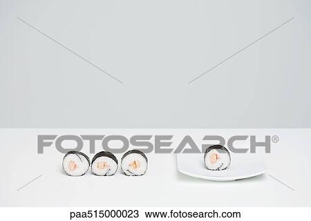Stock Image - Four pieces of maki sushi, three in row on counter, one placed on sushi plate. Fotosearch