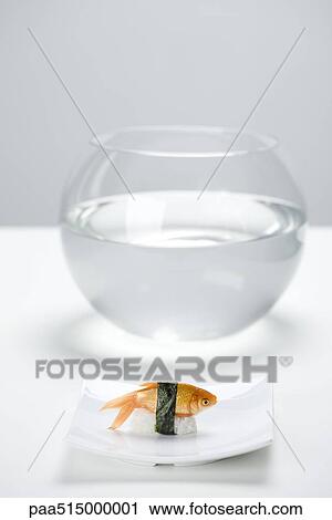 Stock Image - Goldfish prepared as sushi, placed on sushi plate in front of empty fishbowl. Fotosearch