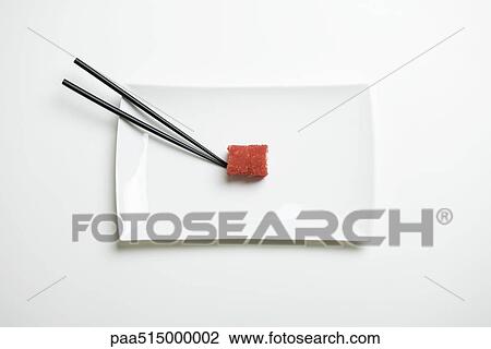 Stock Image - Maki sushi rolled in red flying fish roe beside chopsticks on sushi plate, overhead view. Fotosearch
