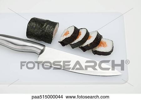 Picture - Partially sliced roll of maki sushi on cutting board with knife. Fotosearch