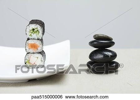 Stock Photograph - Stack of three pieces of maki sushi placed alongside stack of shiny black pebbles. Fotosearch