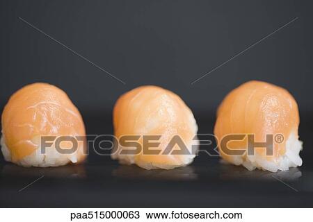 Stock Image - Three pieces of salmon nigiri sushi with dark background, close-up. Fotosearch