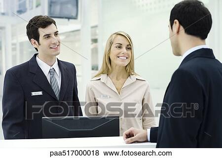 Customer service representatives smiling at businessman waiting at counter View Large Photo Image Stock Photo - Customer service representatives smiling at businessman waiting at counter. Fotosearch