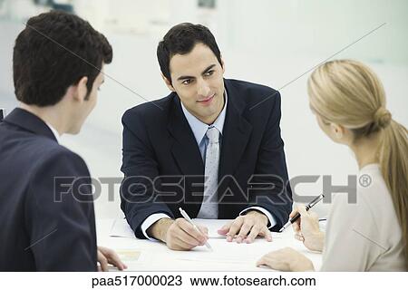 Stock Image - Meeting between professional and clients, woman preparing to sign document. Fotosearch