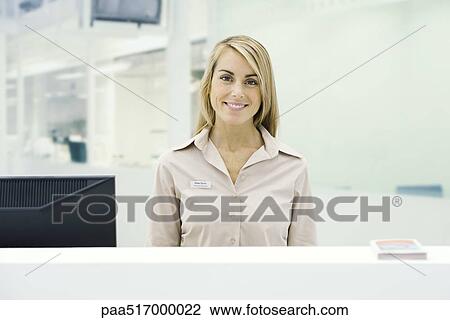 Stock Image - Well dressed woman standing behind counter, smiling at camera, portrait. Fotosearch
