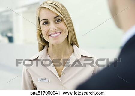 Stock Image - Woman wearing nametag smiling at camera. Fotosearch