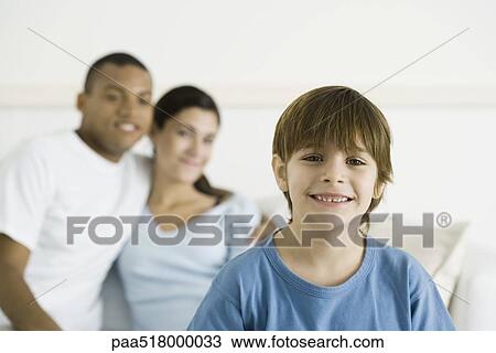 Boy smiling at camera, parents sitting in background View Large Photo Image Stock Image - Boy smiling at camera, parents sitting in background. Fotosearch