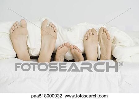 Child lying between parents under comforter, only bare feet sticking out View Large Photo Image Stock Image - Child lying between parents under comforter, only bare feet sticking out . Fotosearch