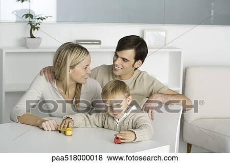 Family at table, boy playing with toy trucks, parents smiling at each other View Large Photo Image Stock Photo - Family at table, boy playing with toy trucks, parents smiling at each other. Fotosearch
