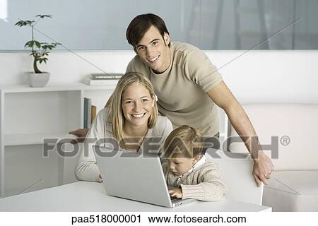 Family gathered around laptop computer, little boy typing, parents smiling at camera View Large Photo Image Stock Image - Family gathered around laptop computer, little boy typing, parents smiling at camera. Fotosearch