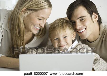 Family gathered around laptop computer, father and son smiling at camera View Large Photo Image Stock Photo - Family gathered around laptop computer, father and son smiling at camera. Fotosearch