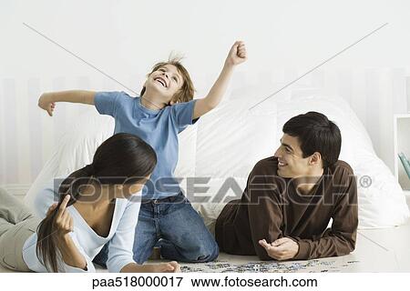 Stock Photo - Family playing with jigsaw puzzle in bedroom, boy laughing, arms raised. Fotosearch