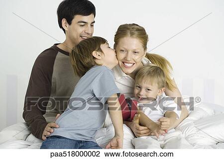 Family sitting together on bed, boy kissing mother's cheek View Large Photo Image Stock Image - Family sitting together on bed, boy kissing mother's cheek. Fotosearch