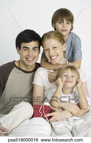 Family sitting together, smiling at camera, mother holding gift View Large Photo Image Stock Photograph - Family sitting together, smiling at camera, mother holding gift. Fotosearch