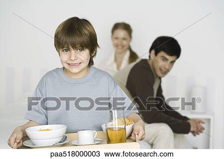 Little boy carrying breakfast on tray, parents sitting on bed in background View Large Photo Image Stock Image - Little boy carrying breakfast on tray, parents sitting on bed in background. Fotosearch