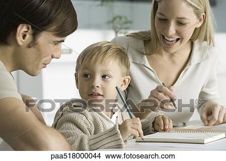 Little boy coloring at table with parents, looking at father View Large Photo Image Picture - Little boy coloring at table with parents, looking at father. Fotosearch