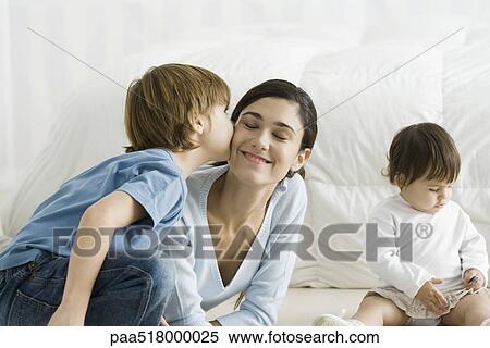 Little boy kissing mother's cheek, toddler girl sitting nearby View Large Photo Image Stock Photography - Little boy kissing mother's cheek, toddler girl sitting nearby. Fotosearch