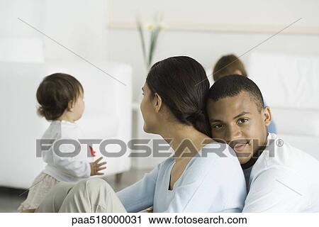 Man embracing wife, smiling at camera, children in background View Large Photo Image Stock Image - Man embracing wife, smiling at camera, children in background. Fotosearch
