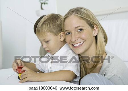 Mother resting her head on son's shoulder, smiling at camera, boy playing with toy cars View Large Photo Image Stock Photograph - Mother resting her head on son's shoulder, smiling at camera, boy playing with toy cars. Fotosearch