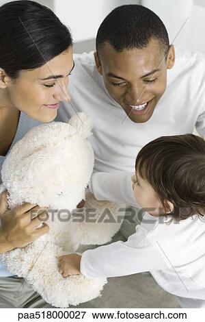 Stock Photo - Parents giving toddler daughter a teddy bear, high angle view. Fotosearch