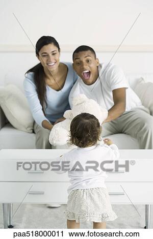 Stock Image - Parents giving toddler girl teddy bear, smiling. Fotosearch