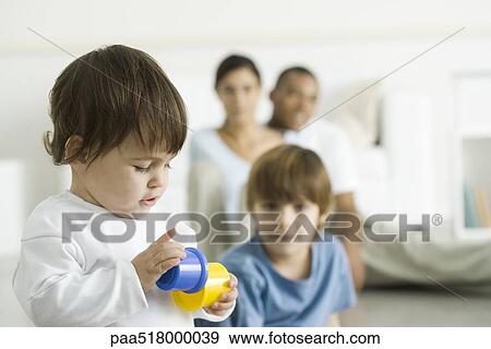Toddler girl playing with toys, family watching in background View Large Photo Image Stock Photo - Toddler girl playing with toys, family watching in background. Fotosearch
