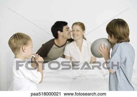 Two boys inflating balloons, parents smiling on bed in background View Large Photo Image Stock Image - Two boys inflating balloons, parents smiling on bed in background. Fotosearch