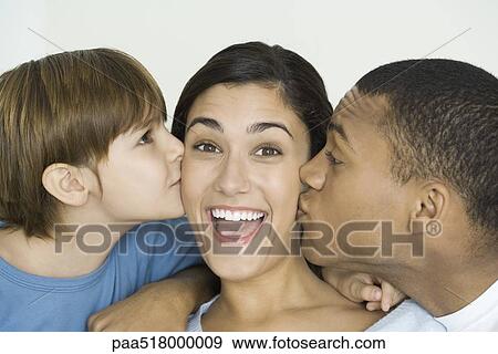 Stock Photo - Woman smiling at camera as husband and son kiss her cheeks. Fotosearch