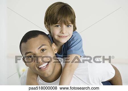 Stock Photo - Young man giving boy piggyback ride, both smiling at camera. Fotosearch
