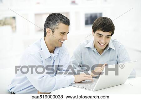 Stock Photo - Father and adult son looking at laptop computer together, smiling. Fotosearch