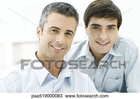 Stock Image - Father and adult son smiling at camera, portrait. Fotosearch