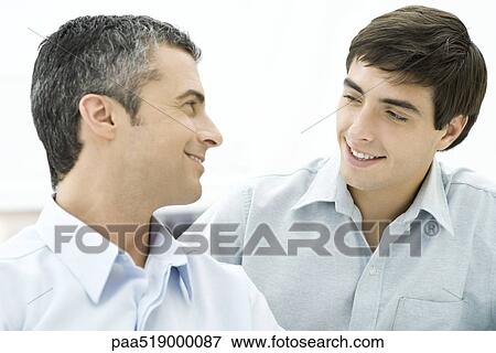 Father looking over shoulder at adult son, both smiling View Large Photo Image Stock Photo - Father looking over shoulder at adult son, both smiling. Fotosearch