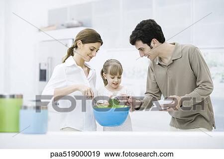 Stock Photo - Little girl helping parents cook in kitchen. Fotosearch