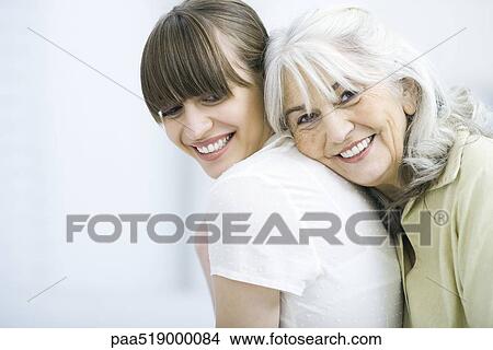 Senior woman leaning against adult daughter's back, smiling at camera View Large Photo Image Picture - Senior woman leaning against adult daughter's back, smiling at camera. Fotosearch