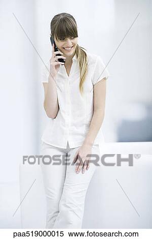 Woman leaning against sofa, using cell phone, smiling View Large Photo Image Stock Photography - Woman leaning against sofa, using cell phone, smiling. Fotosearch