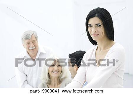 Stock Image - Woman smiling at camera, husband and parents in background. Fotosearch