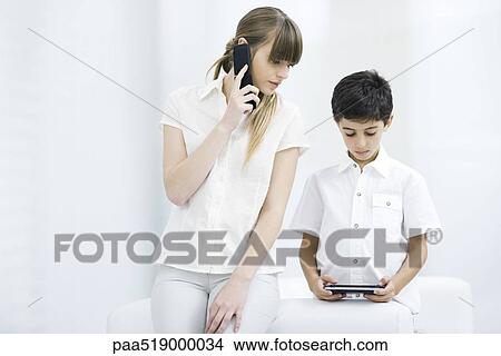 Woman using cell phone, watching boy play handheld video game View Large Photo Image Picture - Woman using cell phone, watching boy play handheld video game. Fotosearch
