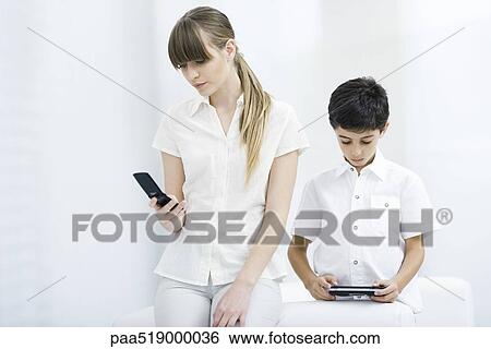 Young woman looking at cell phone while boy plays handheld video game View Large Photo Image Stock Photograph - Young woman looking at cell phone while boy plays handheld video game. Fotosearch