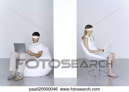 Stock Photograph - Blindfolded man and woman using laptop computers. Fotosearch
