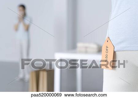 Close-up of sale tag on shirt, woman standing in background View Large Photo Image Stock Photo - Close-up of sale tag on shirt, woman standing in background. Fotosearch