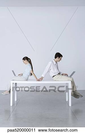 Couple sitting back to back, using laptop computers, holding hands View Large Photo Image Stock Image - Couple sitting back to back, using laptop computers, holding hands. Fotosearch