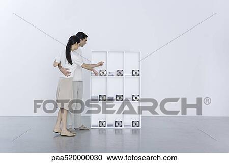 Couple standing beside shelf, pointing at CDs View Large Photo Image Stock Image - Couple standing beside shelf, pointing at CDs. Fotosearch