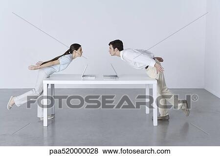 Man and woman at opposite ends of table, leaning towards each other, laptop computers between them View Large Photo Image Stock Photo - Man and woman at opposite ends of table, leaning towards each other, laptop computers between them. Fotosearch