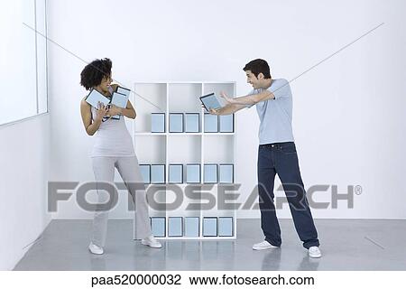 Stock Image - Man and woman joking, fighting over DVDs on shelf. Fotosearch