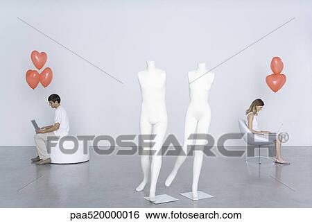 Man and woman sitting with laptops and heart balloons, mannequins in foreground View Large Photo Image Stock Photograph - Man and woman sitting with laptops and heart balloons, mannequins in foreground. Fotosearch